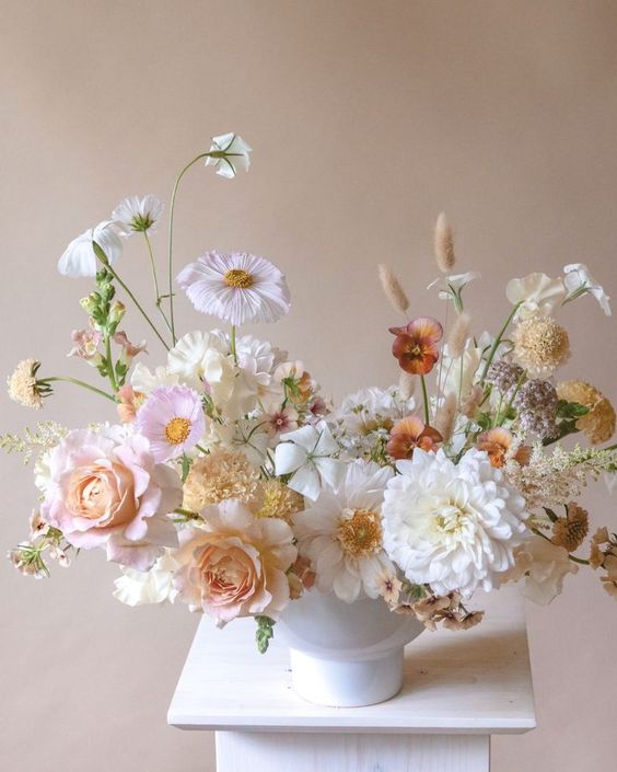 a pretty neutral wedding centerpiece of blush roses and white dahlias, neutral cosmos, forget-me-not and grasses