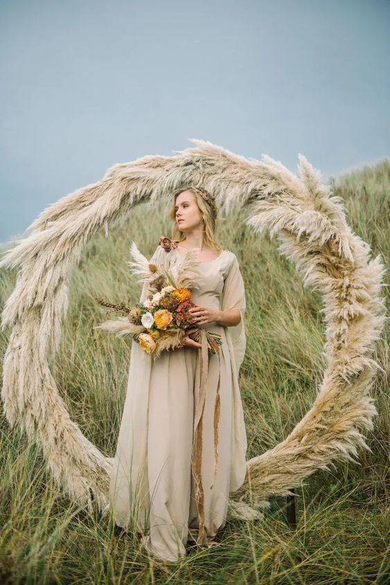a pretty round wedding arch covered with pampas grass is a stylish idea for a boho wedding, great for summer and fall weddings