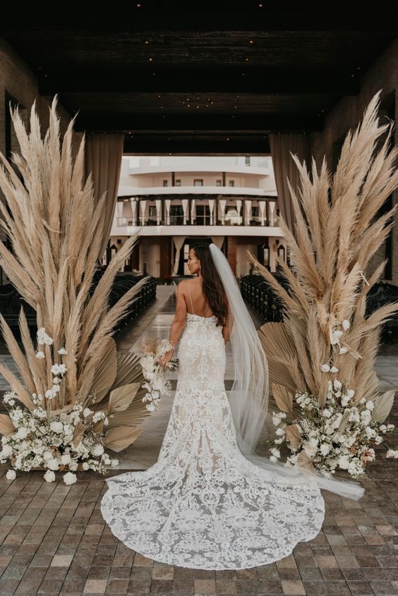 a pretty wedding altar with pampas grass and white blooms plus fronds at the base is a lovely idea for a boho wedding