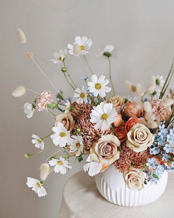 a pretty wedding centerpiece of white cosmos, rust and dusty pink blooms, blue ones and grasses is amazing