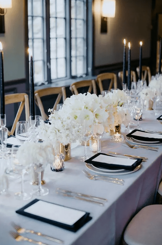 A refined all white winter wedding tablescape with lush blooms and accented with black candles and napkins is awesome