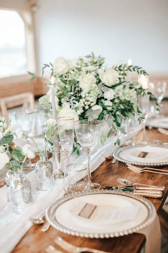 a refined neutral spring wedding table with neutral linens, blooms and greenery, candles and mercury glass vases