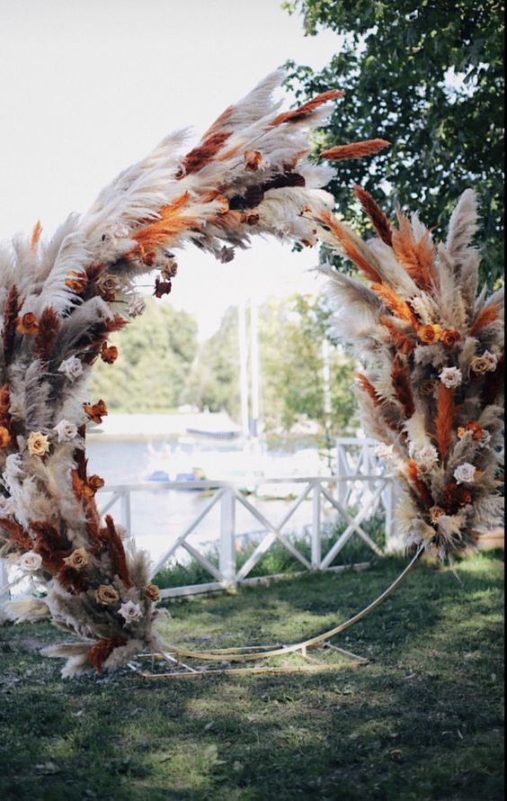 a round boho wedding arch covered with white and orange pampas grass, neutral and bold roses is amazing for a fall boho wedding