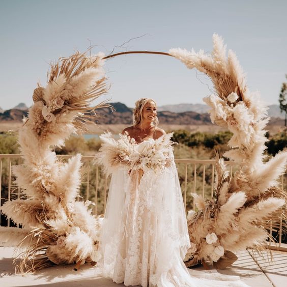 a round boho wedding arch with pampas grass, fronds and some roses is a fantastic idea for a boho wedding in any season