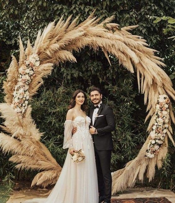 a round pampas grass wedding arch with blush roses is a boho and chic decoration for a wedding