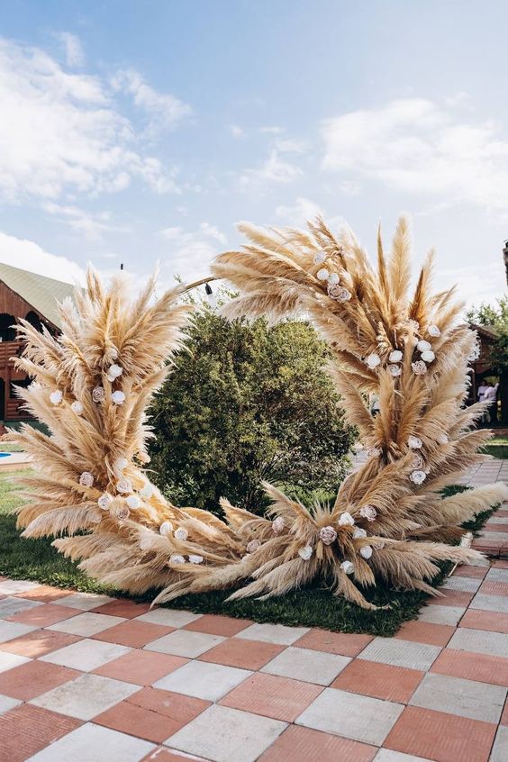 a round wedding arch covered with pampas grass and blush roses is a cool idea for a spring or summer boho wedding