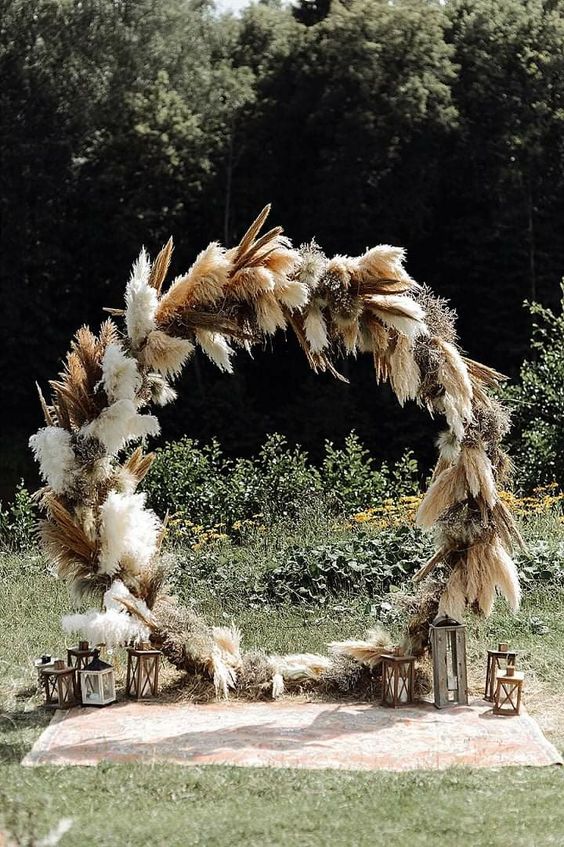a round wedding arch covered with pampas grass and some other grasses is a cool idea for a boho or boho meets farmhouse wedding