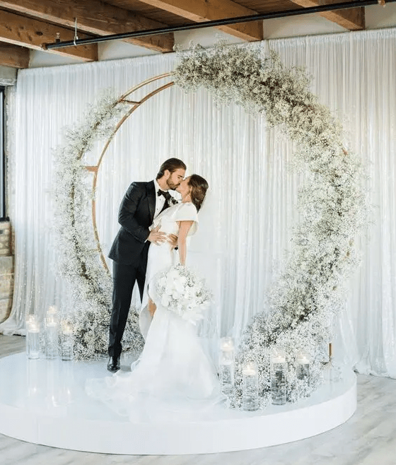 a round wedding arch decorated with white baby’s breath and with floating candles in tall glasses for a modern wedding
