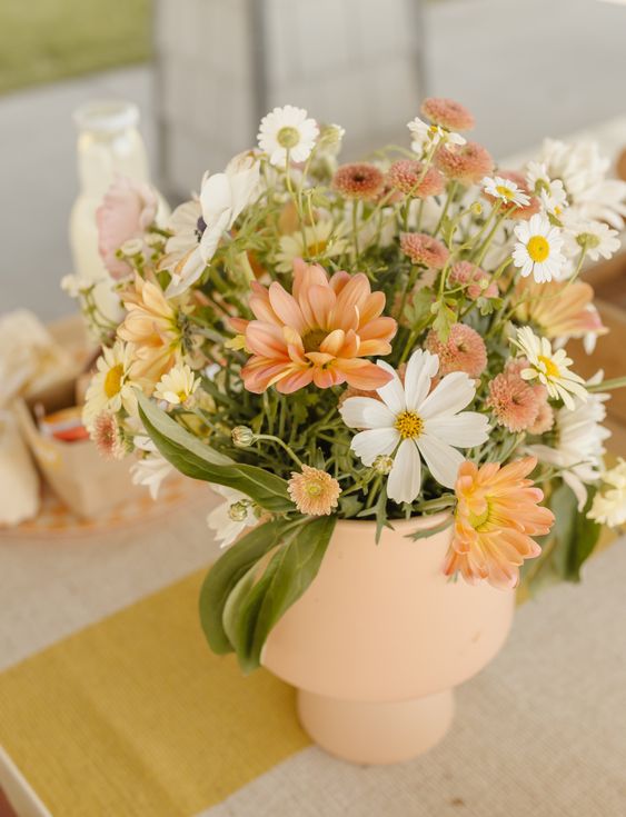 a rustic wedding centerpiece of orange and white cosmos and various fillers and greenery is cool and lovely