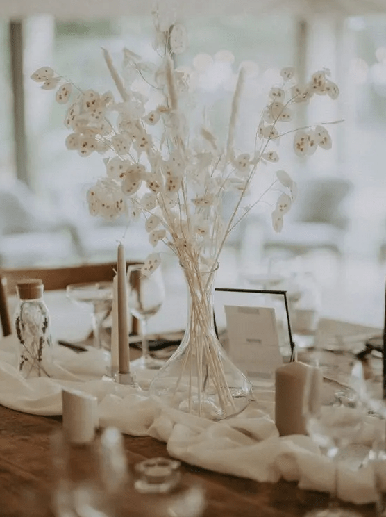 a simple and lovely bleached wedding centerpiece of lunaria and bunny tails plus candles around is a cool idea for a boho wedding