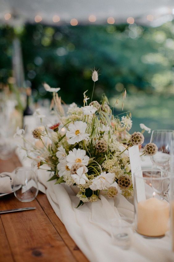 a spring or summer wedding centerpiece of white cosmos and seed pods and grasses is elegant and cool