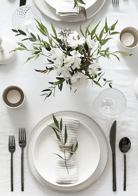 a stylish and simple neutral wedding tablescape with a neutral floral centerpiece, neutral porcelain, black cutlery, candles is chic