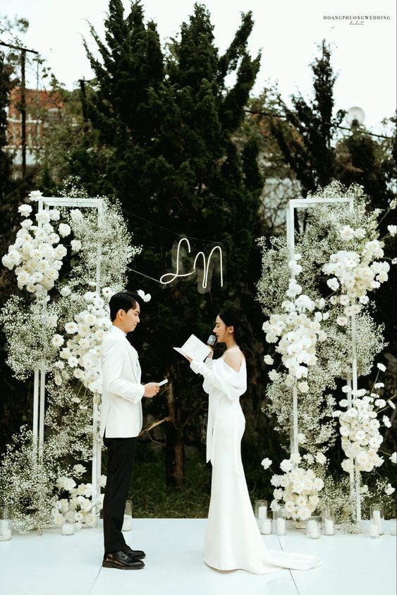 a stylish modern wedding arch of roses, baby's breath and a neon light is a cool and catchy decor idea