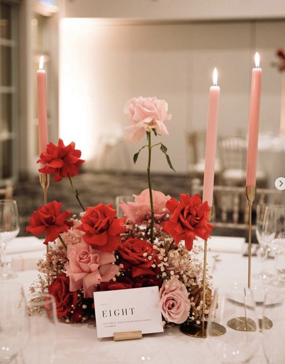 a stylish modern wedding centerpiece of pink and red roses and baby’s breath plus pink candles is a chic and cool arrangement