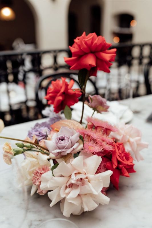 A stylish modern wedding centerpiece of red, blush and lilac roses and some fillers is a very eye catching and bold decoration