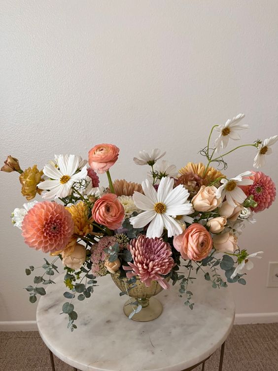 a summer wedding centerpiece of orange dahlias and ranunculus, pale roses, white cosmos and greenery is lovely
