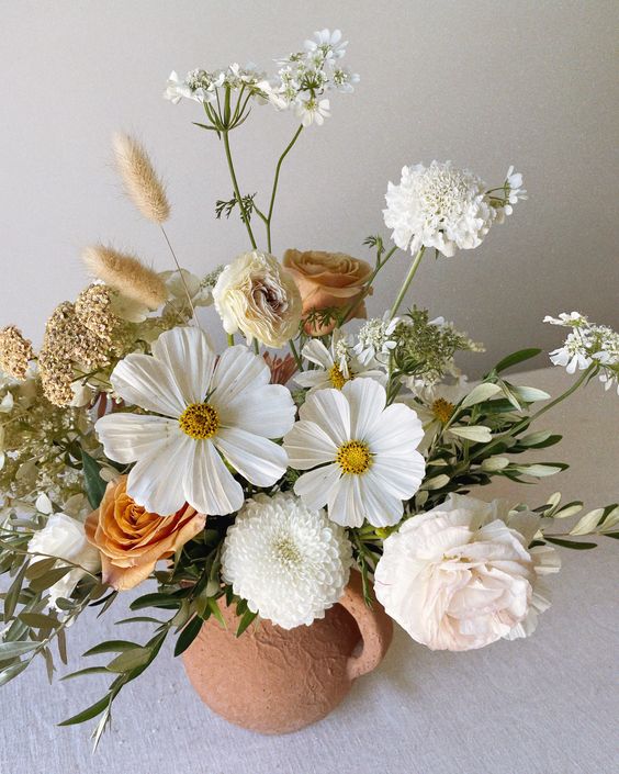 a summer wedding centerpiece of white cosmos, carnations, orange roses and mums, fillers and grasses is cool
