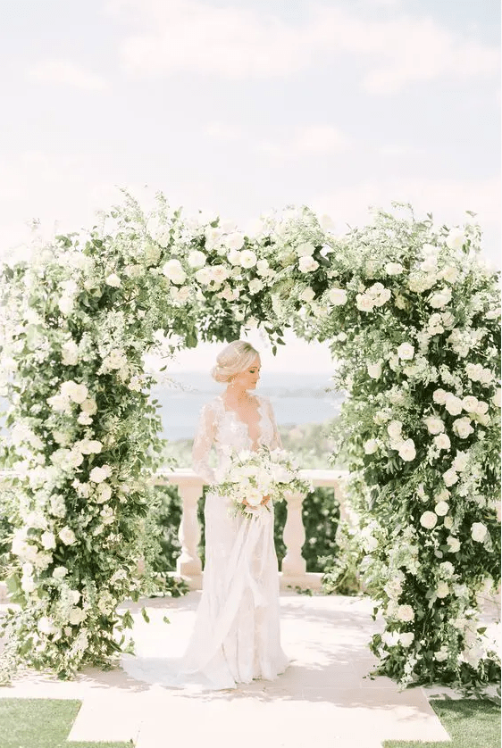 a super lush and chic wedding arch done with greenery and white blooms is a lovely idea for any elegant wedding