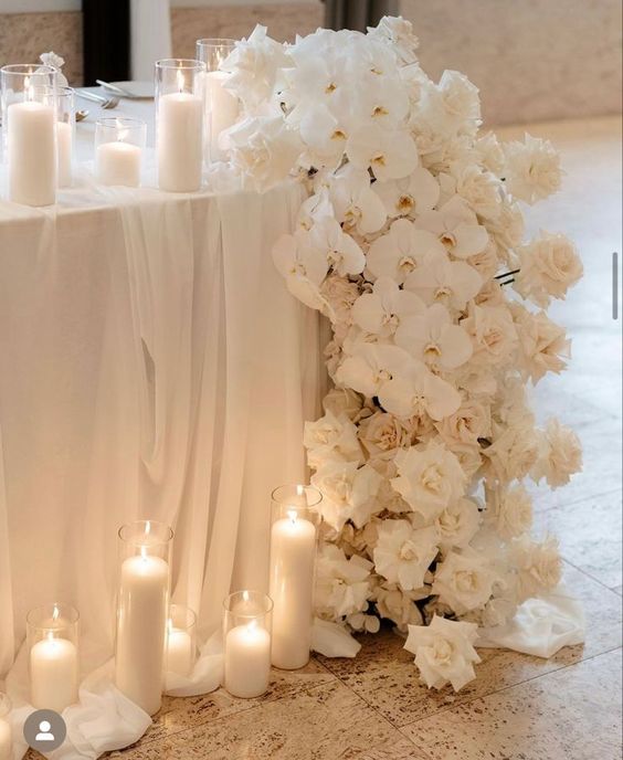 a super lush cascading white wedding centerpiece of roses and orchids and candles around is amazing for a refined wedding