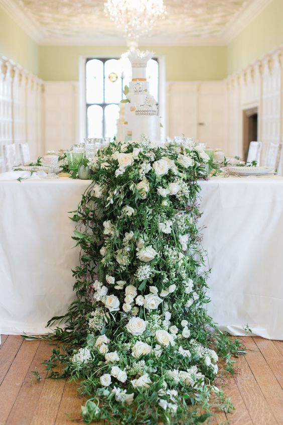 a super lush greenery and white rose wedding centerpiece cascading off the table is a lovely decoration to rock
