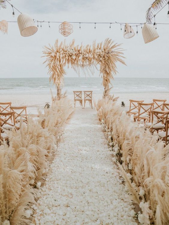 a super lush pampas grass wedding arch with some white blooms and matching arrangements along the aisle is amazing