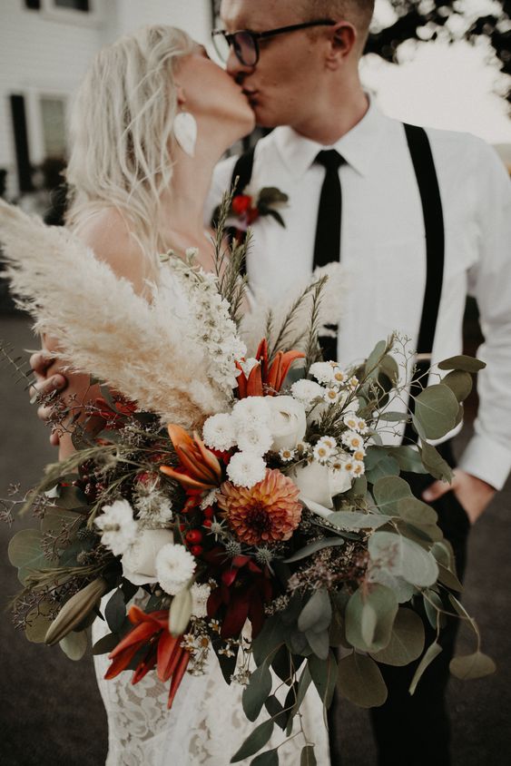 a super lush wedding bouquet of white and orange blooms, greenery, pampas grass and chamomiles as fillers is wow