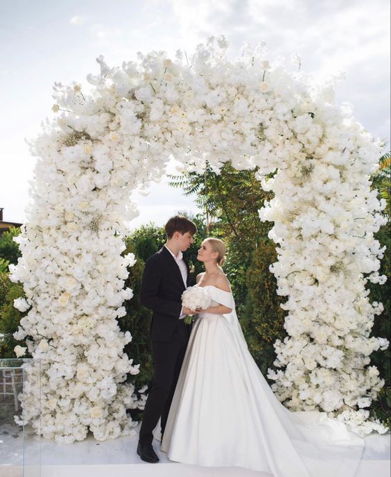 a super lush white wedding arch decorated with hydrangeas, roses and other blooms is a very refined and chic idea