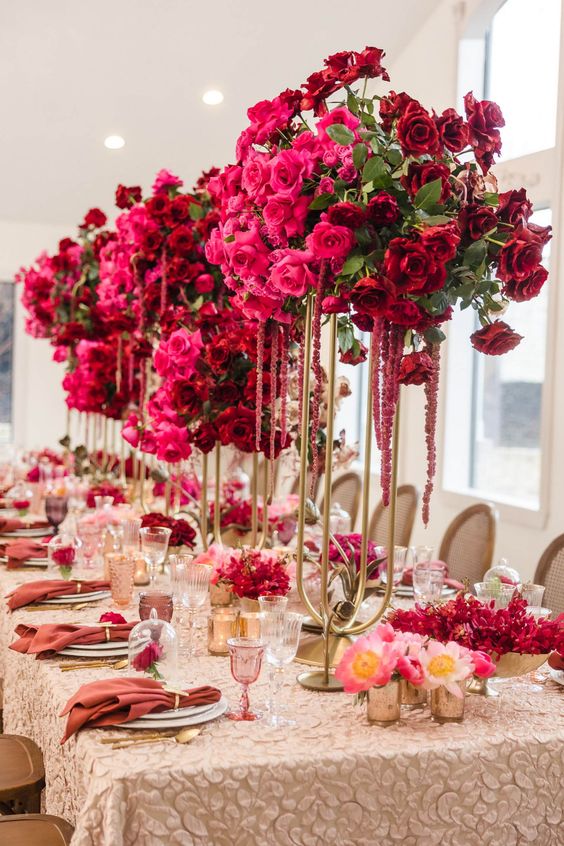 A tall bold wedding centerpiece of red and hot pink roses, greenery and amaranthus is a cool decoration for a color infused wedding