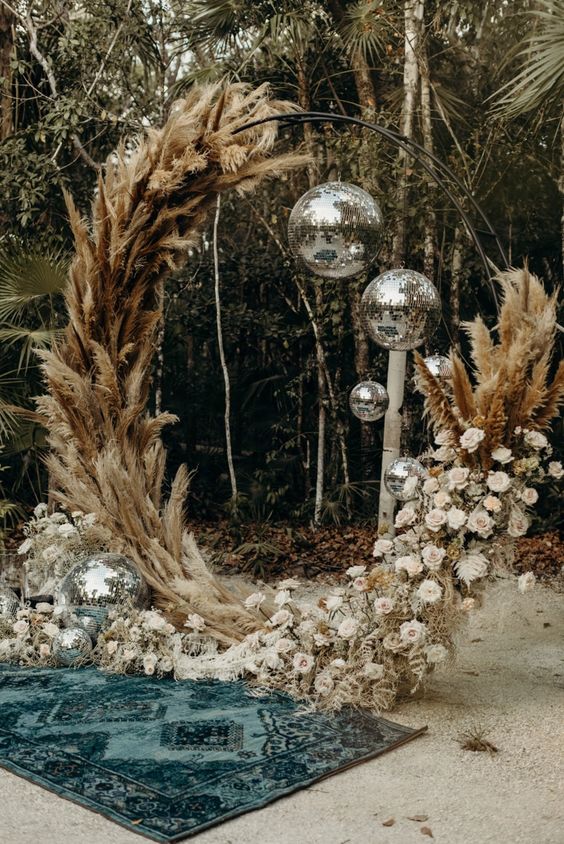 a unique round wedding arch covered with pampas grass and blush roses, disco balls and a boho rug on the ground are amazing for a boho wedding ceremony