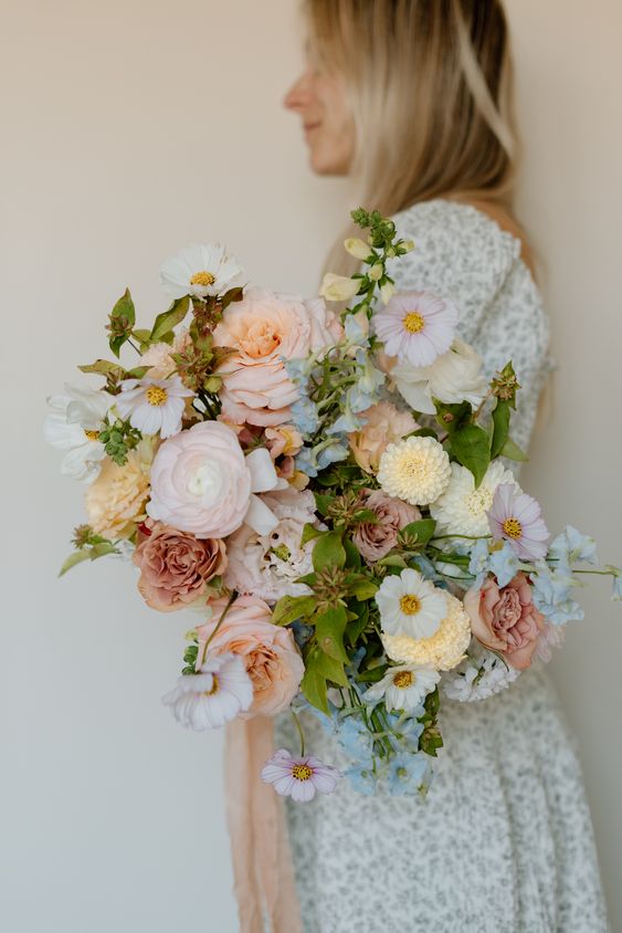 a wedding bouquet of pink and dusty pink roses, yellow mums, pink ranunculus, pink and white cosmos and greenery