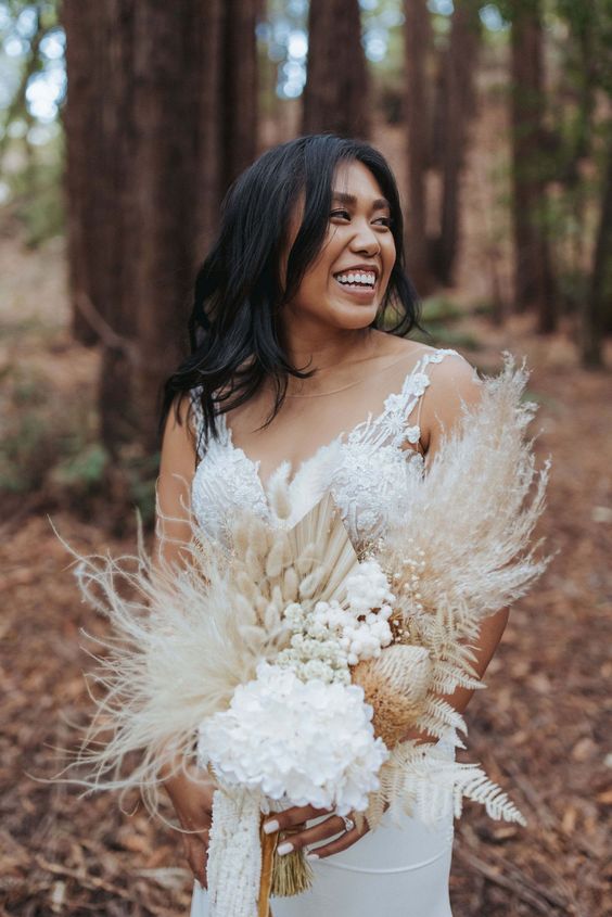 a white boho wedding bouquet of bunny tails, pampas grass, dried blooms and leaves is a stylish and cool idea
