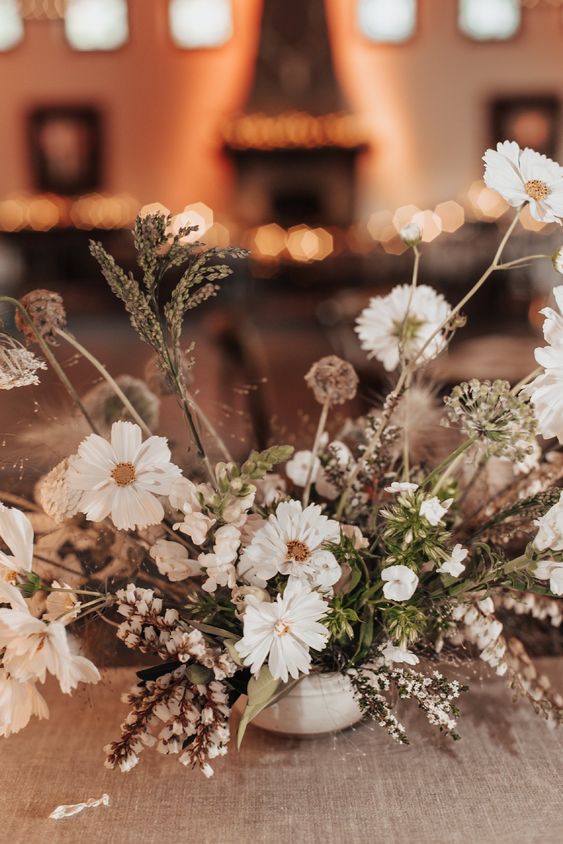 a white textural and dimensional wedding centerpiece of cosmos, seed pods, fillers and grasses is cool for summer