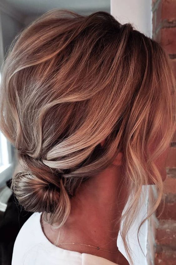 a wrapped low bun, a messy wavy bump on top and face-framing hair is a cool and stylish hairstyle for a wedding