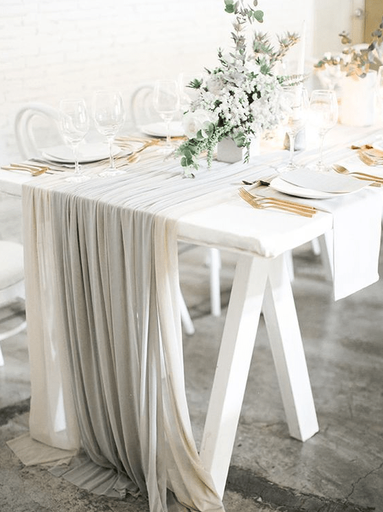 an airy and chic Scandinavian table setting with white and grey linens, gold cutlery, pale greenery and white blooms