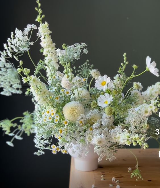 an airy wedding centerpiece of white cosmos, mums, chamomiles and some greenery and blooming branches for spring or summer