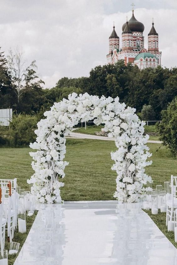 an all-white wedding arch with lots of white blooms and vines spray painted white to make the arch look like it's frozen