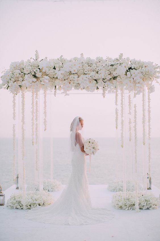 an elegant white wedding chuppah with roses, orchids, some hanging blooms and blooms on the floor is a cool idea