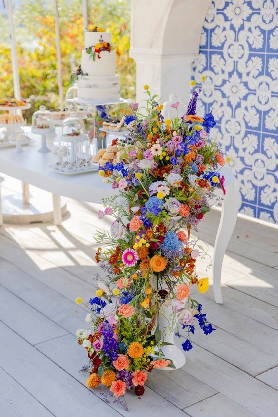 an extra bold cascading wedding centerpiece of pink, orange, yellow, blue and purple blooms and greenery for a boho wildflower wedding