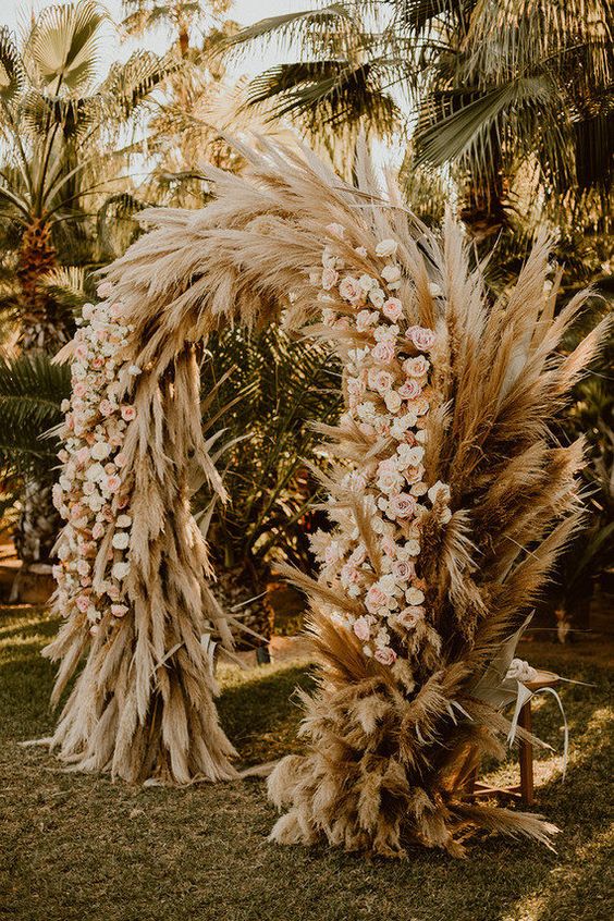 an extra lush boho wedding arch covered with pampas grass and blush roses is a cool idea for a summer boho wedding