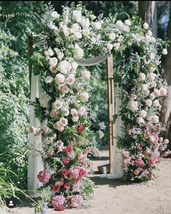 an ombre wedding arch from red and pink to white and with greenery is a very lush decoration for a garden wedding