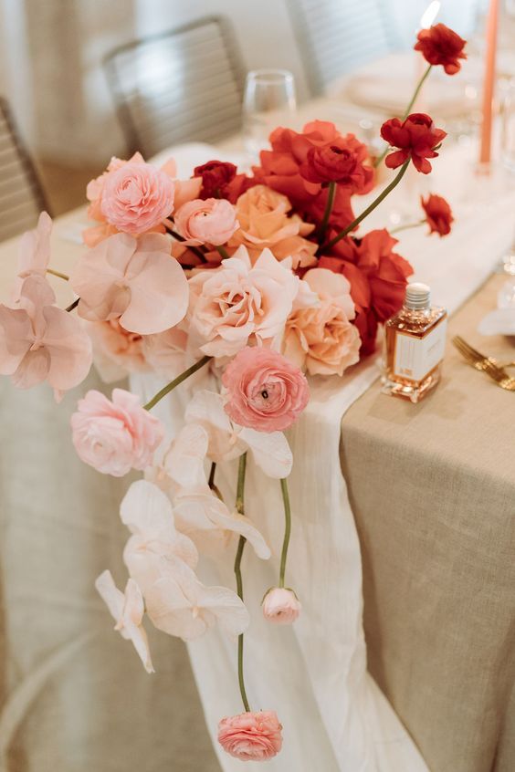 an ombre wedding centerpiece from blush to peachy and deep red, of orchids, ranunculus and roses is a gorgeous modern wedding idea