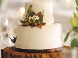 a white wedding cake decorated with bold fall leaves, blooms and a couple of acorns is a chic idea for a modern fall wedding