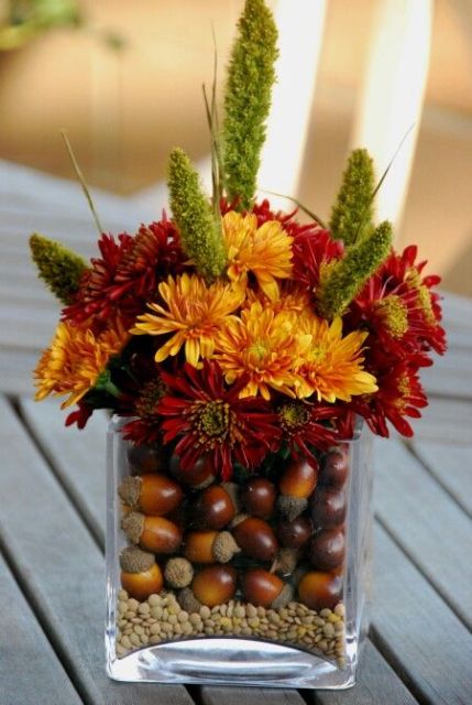 a fall wedding decoration or a centerpiece of a glass filled with acorns, bold blooms and twigs is a cool idea that you can easily DIY
