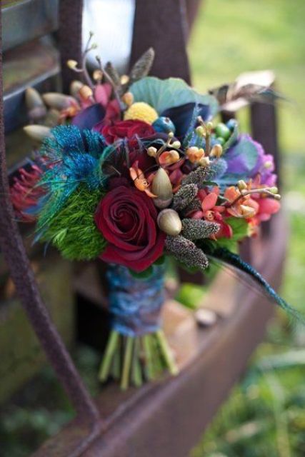a jewel tone wedding bouquet of bold blooms, greenery, feathers and acorns is a gorgeous idea for a bright fall wedding