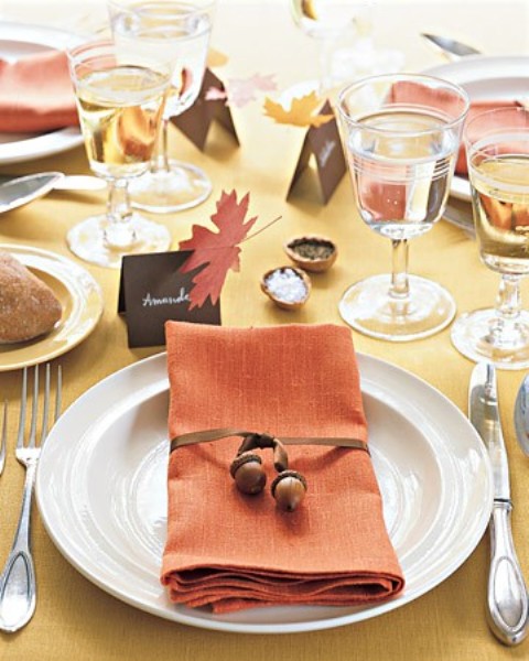 a fall wedding tablescape with a mustard tablecloth, bold fall leaves, an orange napkin and bold fall leaves, acorn napkin rings is fun and bright