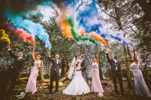 a wedding photo in the forest accented with lots of colorful smoke bombs instead of usual confetti or petals