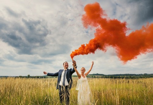 a beautiful wedding portrait in the field with an orange smoke bomb is a lovely and fun idea for a wedding