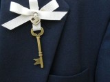 a refined wedding boutonniere of a vintage key, a mini heart-shaped lock and a white ribbon bow