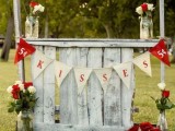 a rustic wedding kissing booth of pallet and wood, with a fabric bunting, some bright blooms