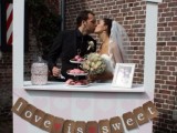 a pale pink and white heart print wedding kissing booth with a burlap bunting and a bold sign on top
